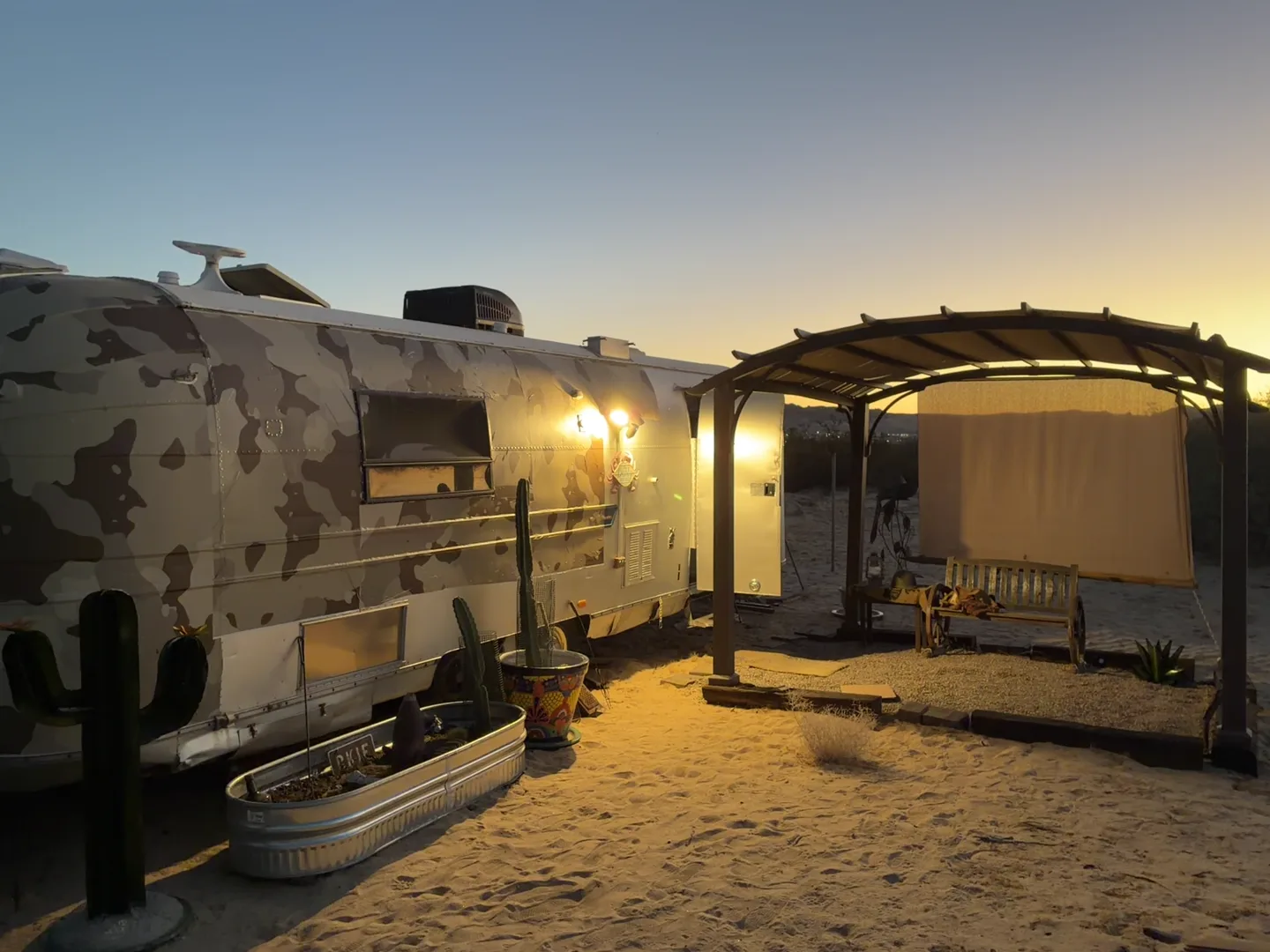The Camp Warner pergola and trailer lit warmly at dusk
